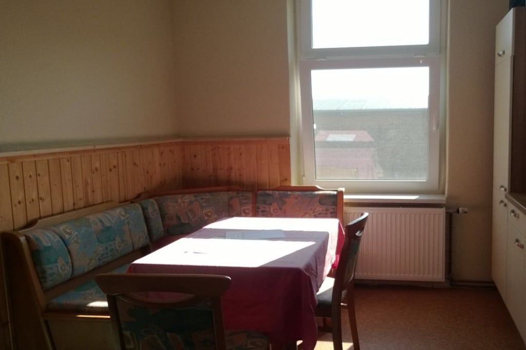 A corner room with a wooden bench, a table with a white tablecloth, and a window with a view.
