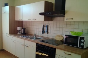 A kitchen with white cabinets, a stove, a microwave, and a sink. - Holiday apartment with 1 bedroom (Zehdenick)