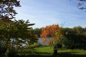 A garden with a lawn, a tree with autumn leaves, and a body of water in the background. - Holiday apartment with 1 bedroom (Zehdenick)