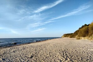 A beach with footprints leading to the water, a clear sky, and a grassy hill in the background. - Holiday apartment with 1 bedroom (Dranske)