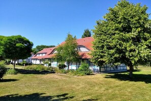 A traditional house with a red roof, surrounded by a well-maintained lawn and trees. - Holiday apartment with 1 bedroom (Dranske)