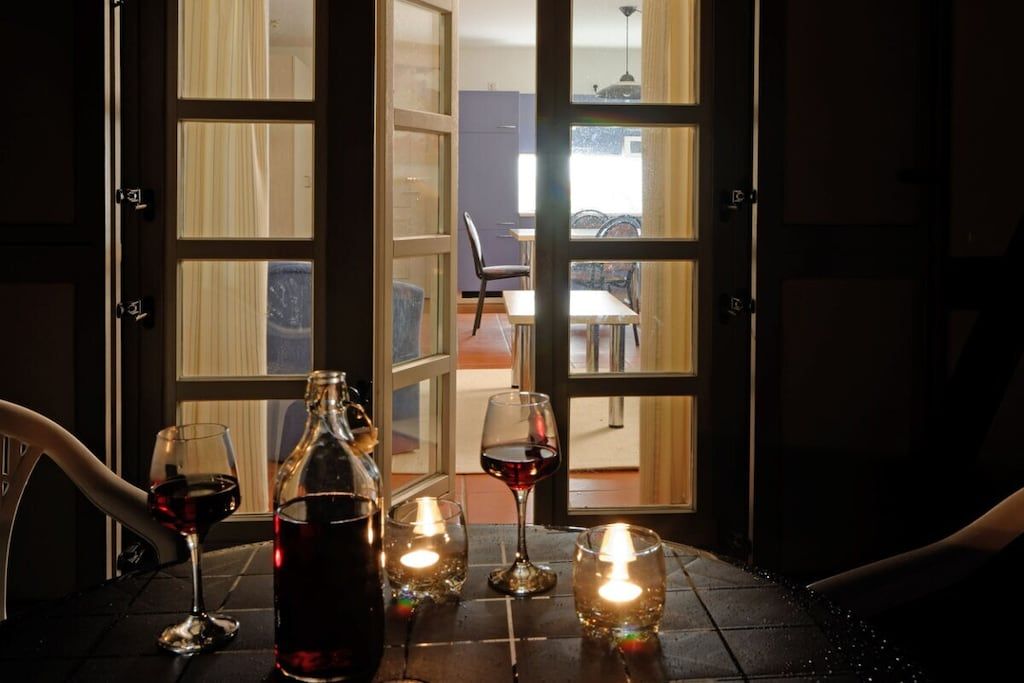 A table with a bottle and glasses of red wine, a candle, and a view through a glass door into a dining area.