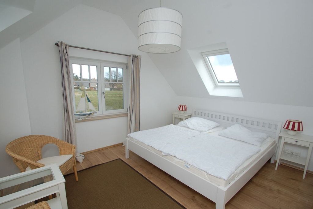 A bedroom with a single bed, a window, a chair, and a bedside table with a lamp.