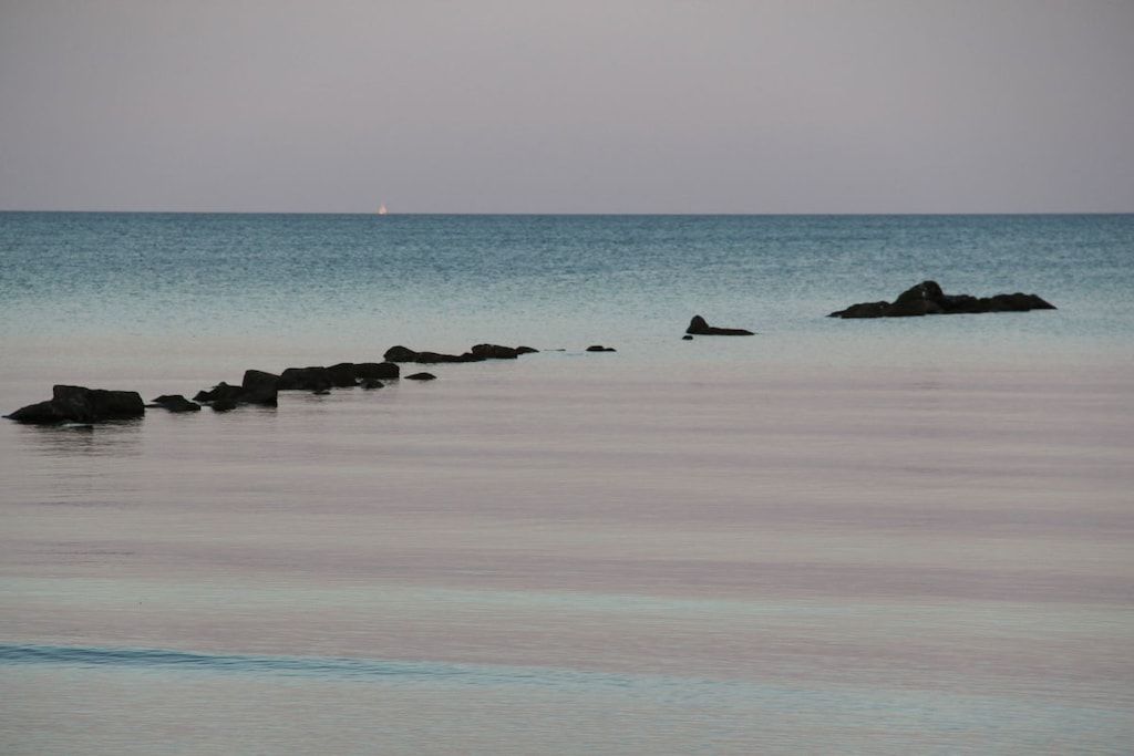 Mar calmo com rochas e um navio ao longe.