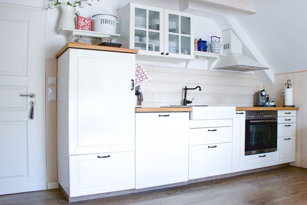 Una cocina con armarios blancos, horno empotrado y encimera de madera.