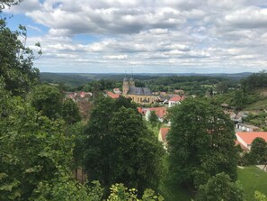 A town with a prominent church featuring a tall steeple, surrounded by lush greenery and rolling hills in the background.
