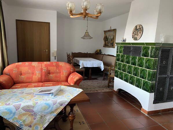 A living room with a sofa, a table with a floral tablecloth, a chandelier, a painting, and a tiled fireplace.