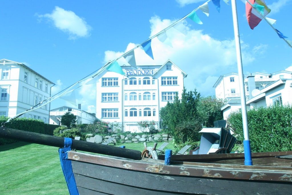 A building with a large sign reading 'FEODORA' in front of a well-maintained lawn and a row of trees.