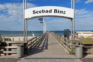Ein hölzerner Steg führt zu einem Strand, auf dem ein Schild 'Seebad Binz' steht.