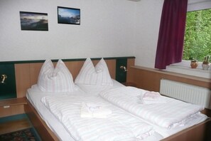 Ein Doppelbett mit gestreifter Bettwäsche, ein Kopfteil mit grüner Bordüre und zwei gerahmte Bilder an der Wand.