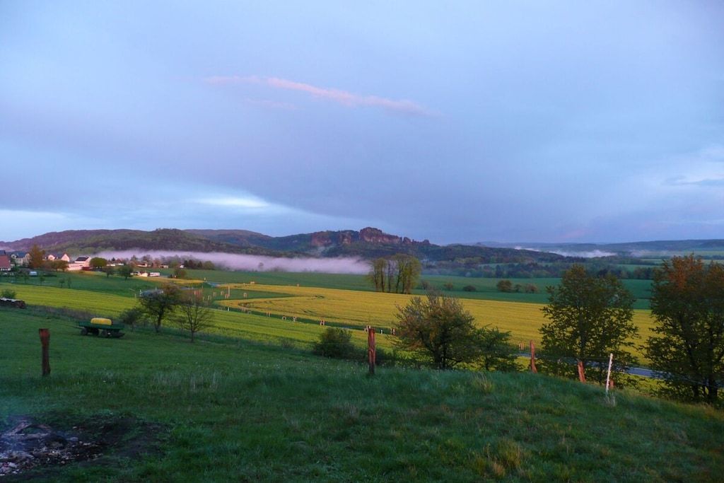 Ländliche Landschaft mit sanften Hügeln, Feldern und einer kleinen Siedlung in der Ferne.