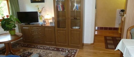 Un salon avec un téléviseur, un meuble en bois et un tapis à motifs.