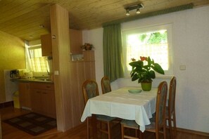 Uma área de refeições com mesa posta para quatro pessoas, um vaso de plantas e uma janela com cortinas.