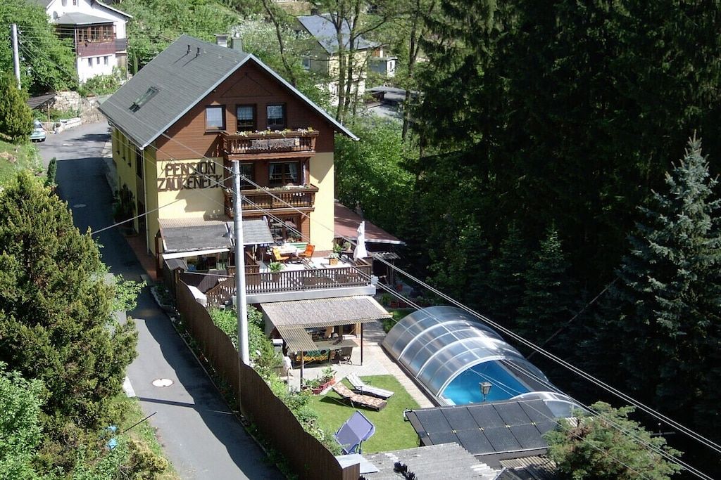 A two-story building with a balcony, a swimming pool, and a greenhouse structure.