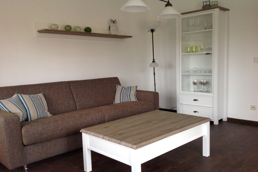 Una sala de estar con un sofá marrón, una mesa de centro blanca, un aparador blanco con puertas de vidrio y una lámpara colgante.