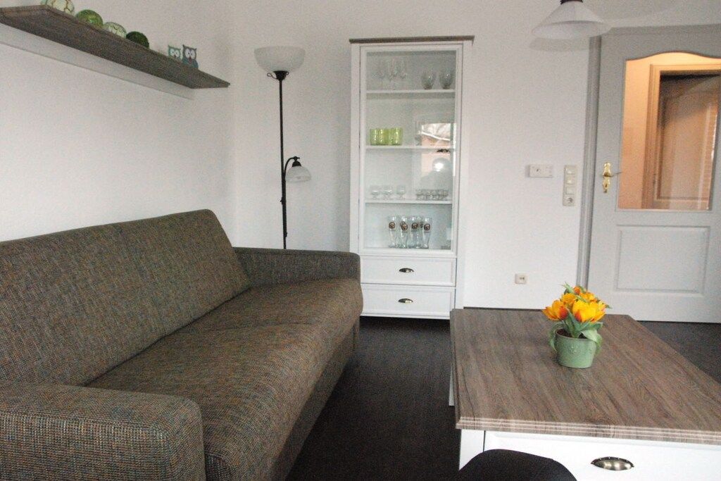 Een woonkamer met een bank, een kast met glazen deuren, een tafel met een bloemenvaas en een lamp.