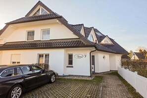 Ein zweistöckiges Haus mit einem Ziegeldach, einer Auffahrt und einem weißen Zaun.