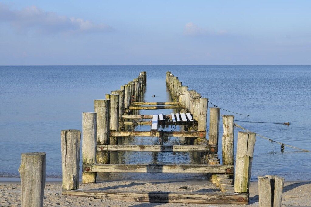 A wooden pier extending into calm water with a clear sky above.