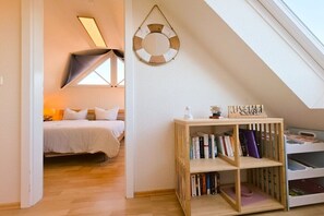 Ein Schlafzimmer mit schrägem Dach, einem Bett, einem Nachttisch mit Büchern und einem an der Wand befestigten Regal.
