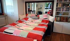 Ein Schlafzimmer mit einem Bett, einem Bücherregal und Blick ins Freie.