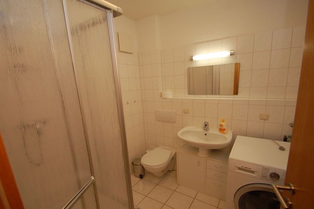 Casa de banho com chuveiro, sanita, lavatório e máquina de lavar roupa.