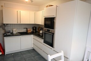 A kitchen with white cabinets, a black countertop, a microwave, and an oven. - Holiday home in Prerow with swimming pool (Prerow)