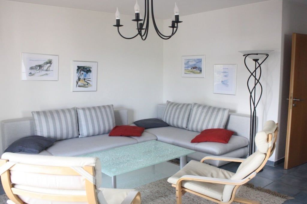 A modern living room with a sofa, armchairs, a glass coffee table, and artwork on the walls.