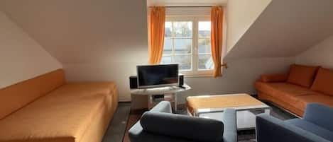 Ein Loft-Zimmer mit geneigter Decke, einer Couch, einem Couchtisch und einem Fernseher.