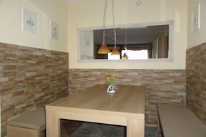 A dining area with a wooden table, cushioned bench seating, a vase with flowers, and pendant lighting. - Holiday apartment in Damp with swimming pool (Damp)