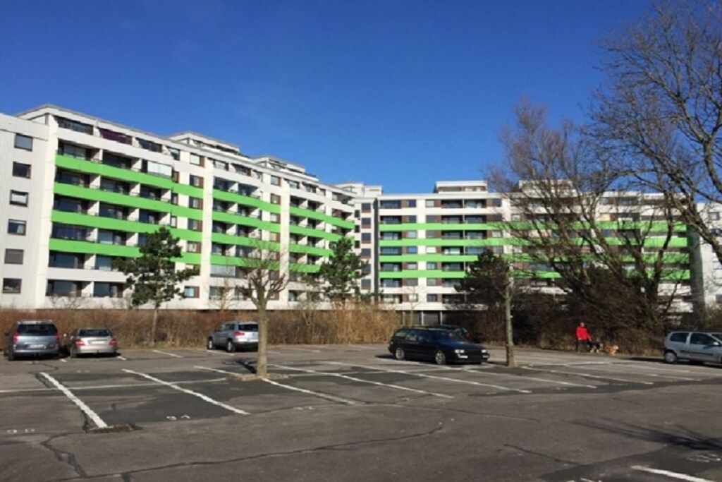 Un parking à plusieurs étages, situé à côté d’un bâtiment orné de bandes horizontales vertes.