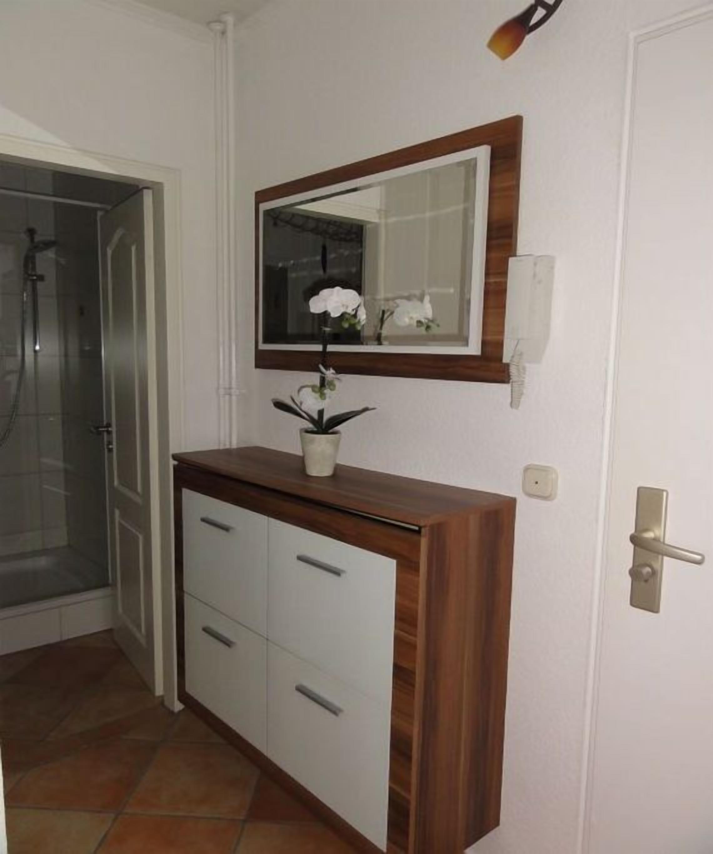 A bathroom with a wooden vanity, a mirror, a potted orchid, and a shower area.