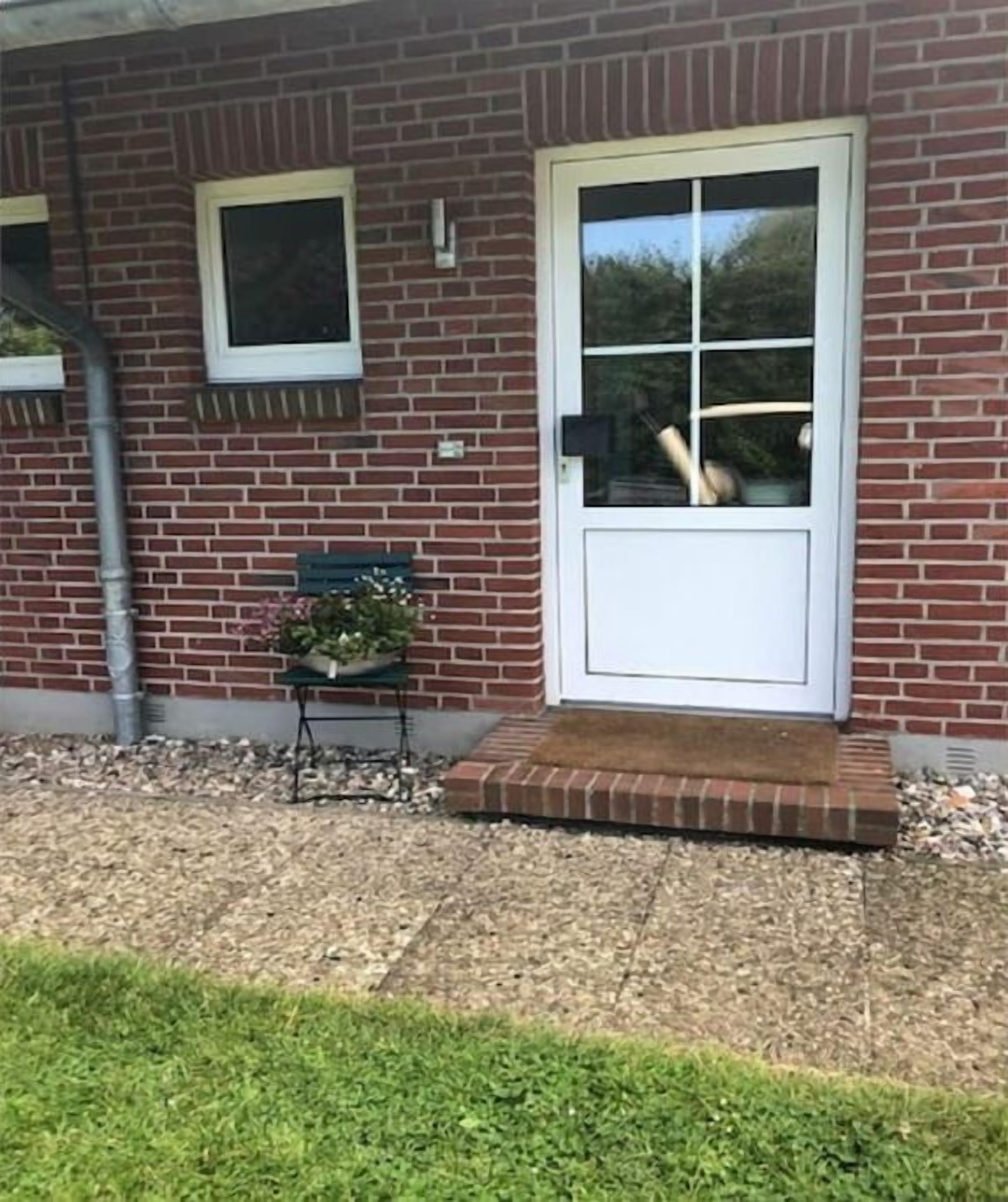 Ein Backsteinhaus mit weißer Tür und Fenstern, ein kleiner Tisch mit einer Pflanze und ein Schotterweg.
