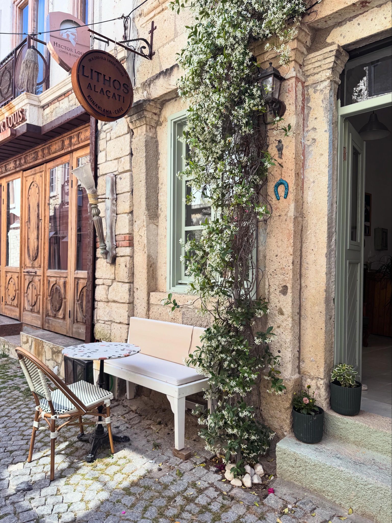 Un café con una banca de madera y una mesa al aire libre, un letrero colgante y una pared cubierta de plantas trepadoras.