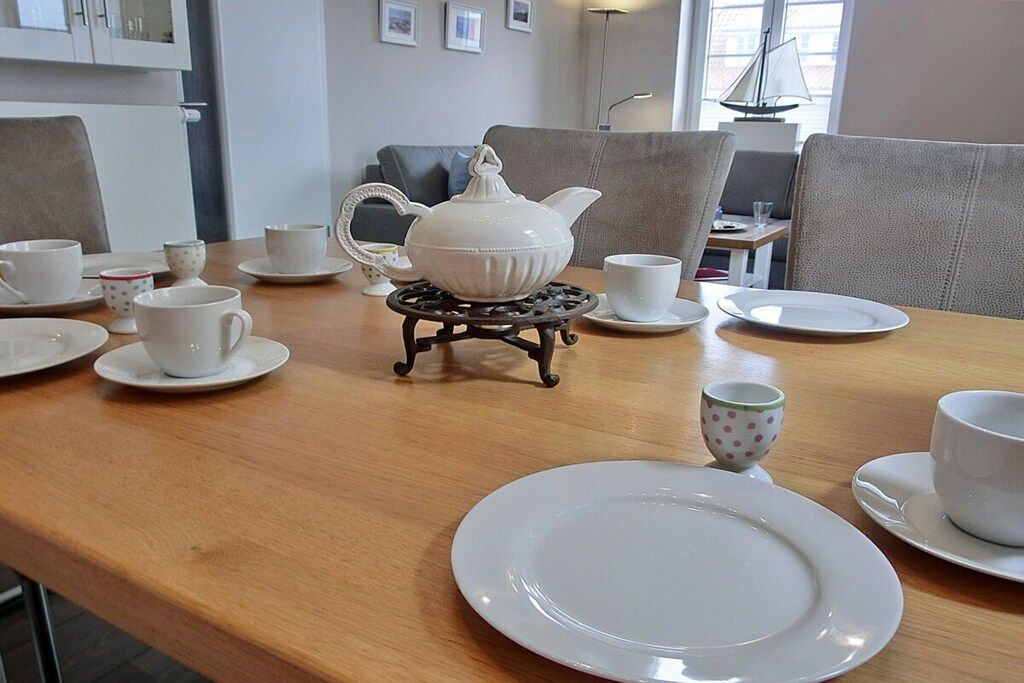 A dining table set with white plates, cups, and a teapot on a small stand.