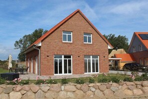 A two-story brick house with a sloped roof, large windows, and a stone wall in front. - Holiday home Strandrose (Rerik)