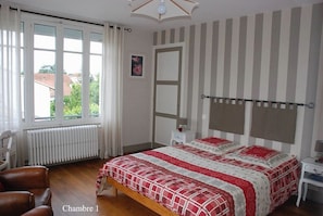A bedroom with a large bed, a radiator, a window with curtains, a chair, and a bedside table. - Vrbo Property (Romans-sur-Isère)