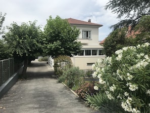 A residential street with a house, a paved path, and lush greenery.