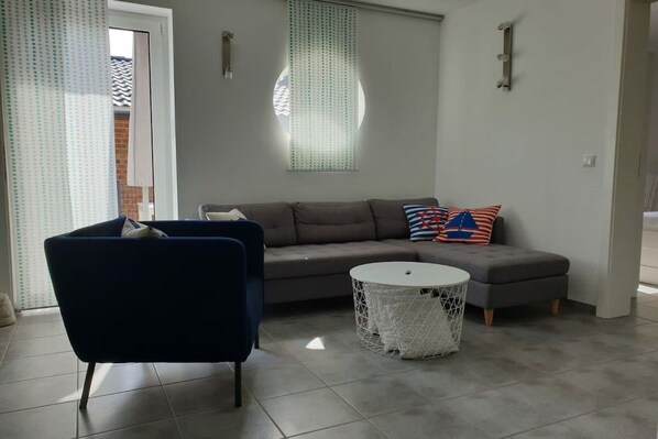 Una sala de estar moderna con un sofá, un sillón azul, una mesa de centro redonda y un panel decorativo en la pared.
