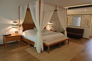 A bedroom with a four-poster bed, bedside lamps, a bench, and a patterned wall divider.