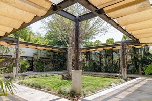 A covered outdoor area with a concrete floor, surrounded by lush greenery and a stone wall.