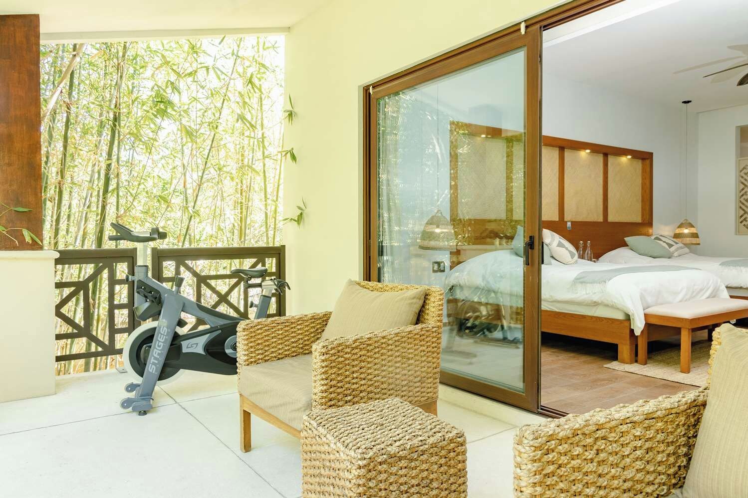 Une chambre avec un lit, une porte-fenêtre coulissante donnant sur un balcon et un vélo d’appartement.