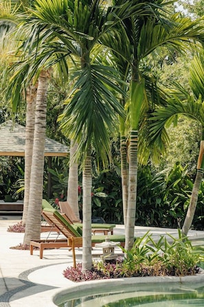 A pool area with palm trees, lounge chairs, and a stone lantern.