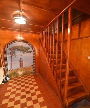 A wooden staircase with a checkered floor leading to a door with a mural of a tree and a tower. - Rhododendron OG || Prerow (Prerow)