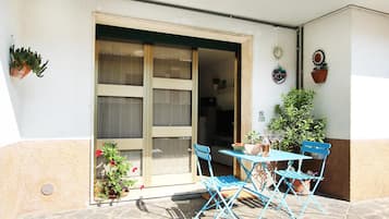 Eine Terrasse mit Tisch und Stühlen, Blumentöpfen und einer Schiebetür zu einem Innenraum.