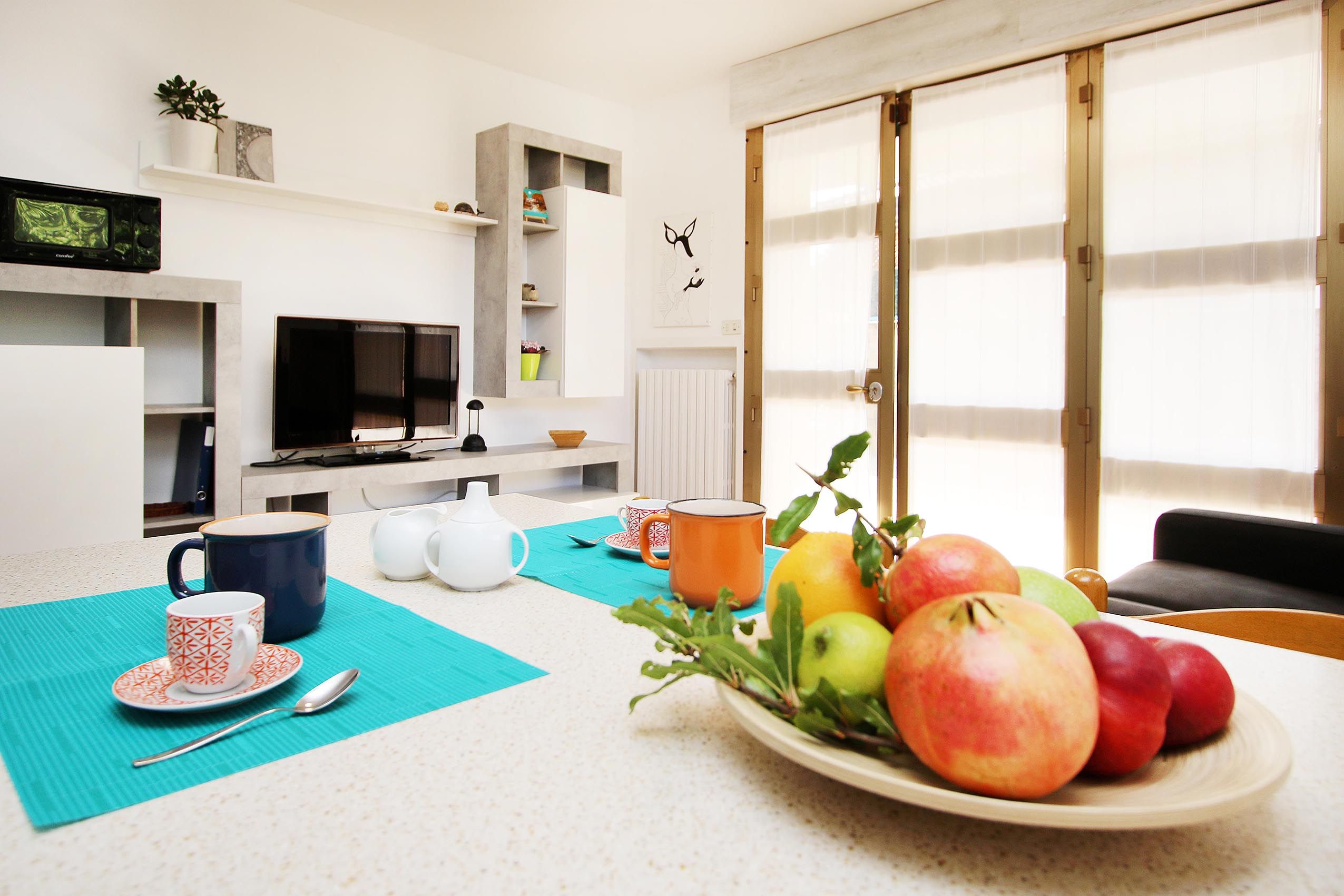 A modern living room with a dining area, a television, and a fruit bowl on the table.