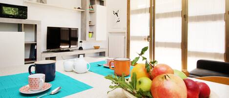 A modern living room with a dining area, a television, and a fruit bowl on the table.