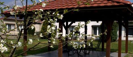 Un gazebo con tetto in tegole, circondato da un prato e un edificio sullo sfondo.
