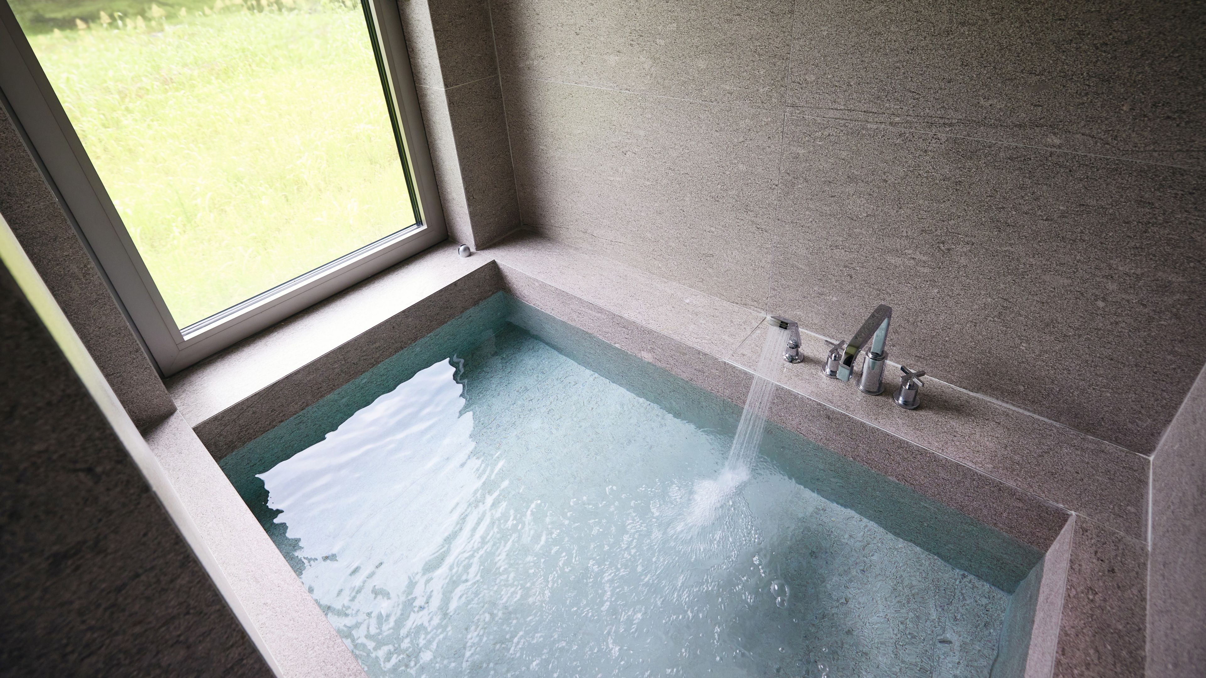 A bathtub with a faucet and a window above it.