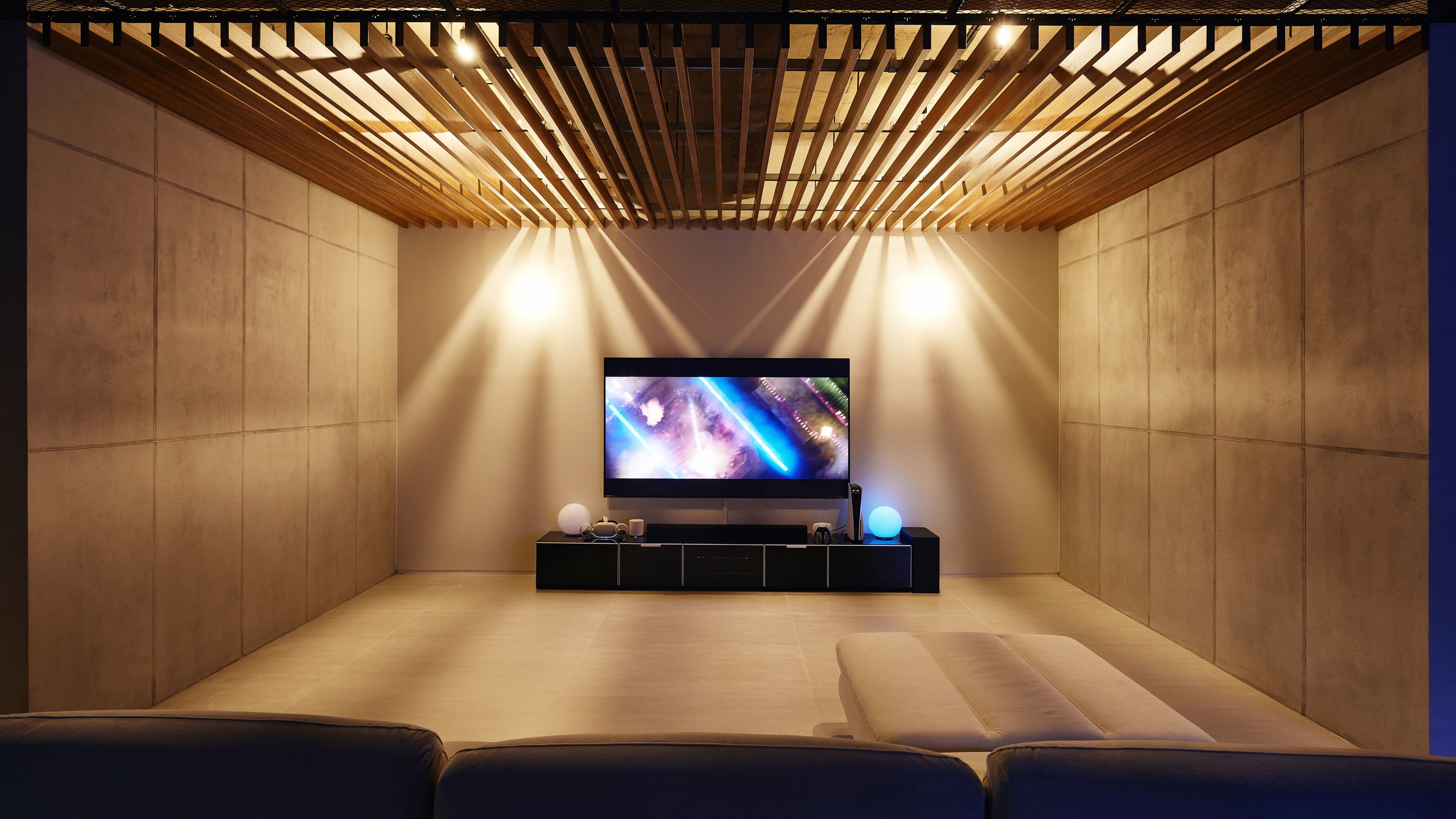 A modern cinema room with a flat-screen TV, wooden slats overhead, and a cushioned seating area.