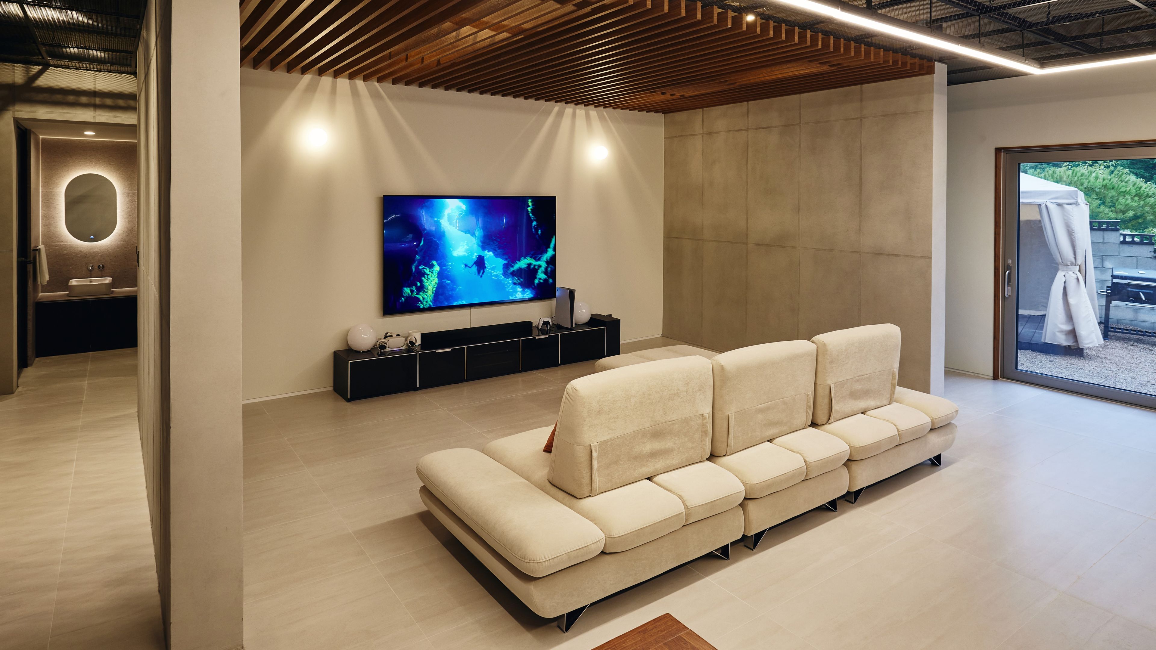 A modern living room with a large flat-screen TV, a beige sectional sofa, and a minimalist design.